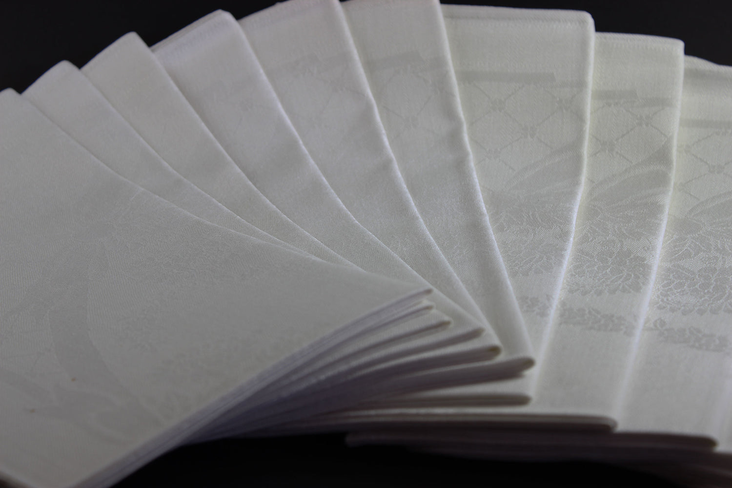 Twelve white damask Irish linen napkins on black background.