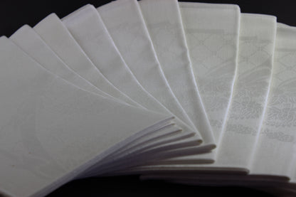 Twelve white damask Irish linen napkins on black background.