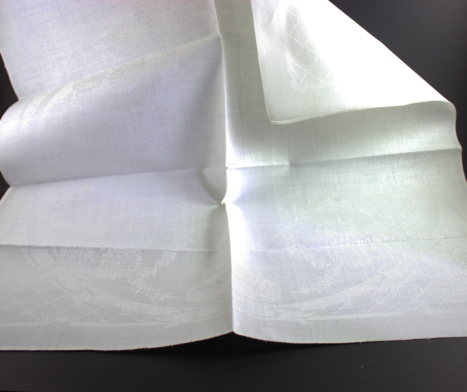 Unfolded white damask Irish linen napkin on black background.