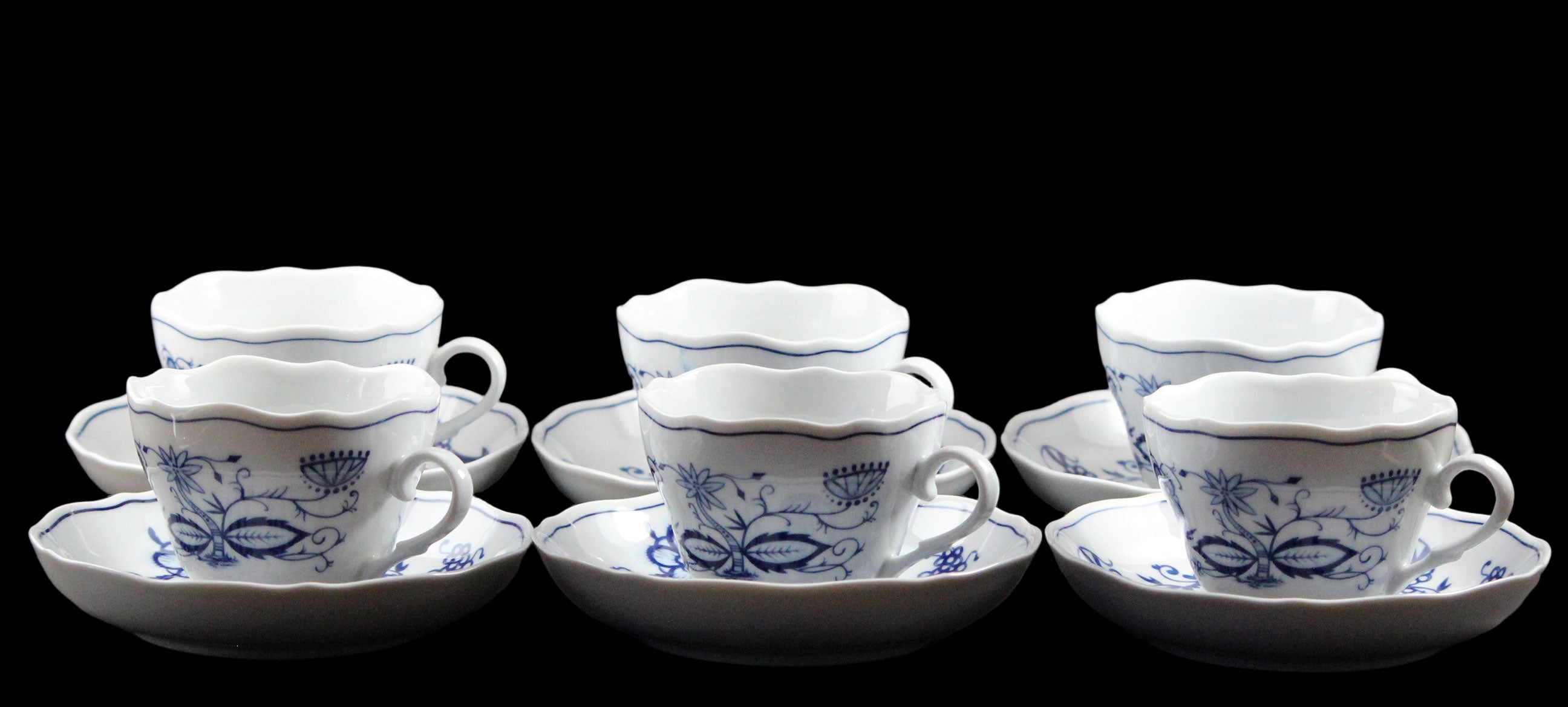 Set of ceramic teacups and saucers with blue floral patterns on a dark background