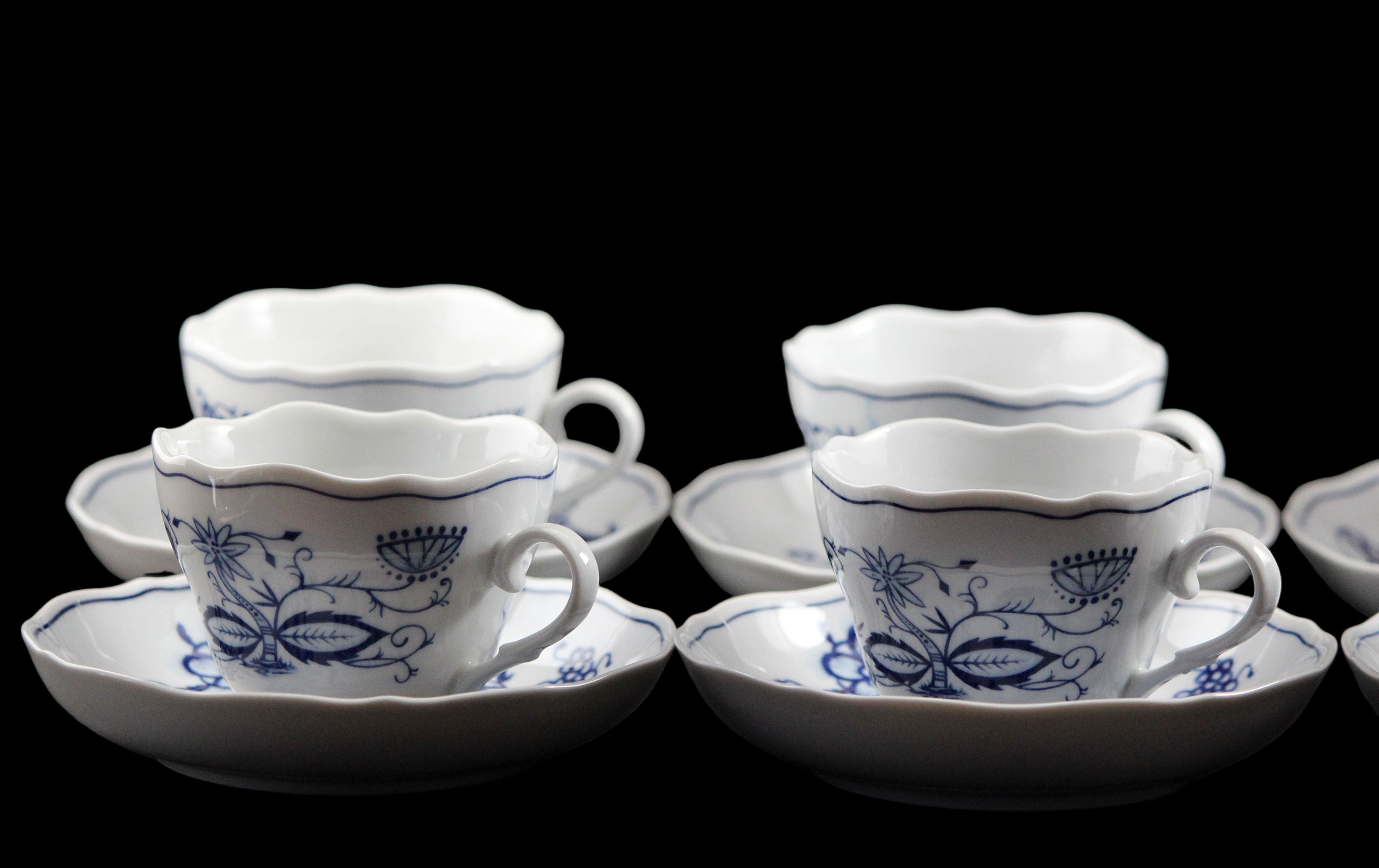 Set of white ceramic teacups and saucers with blue floral patterns on a dark background