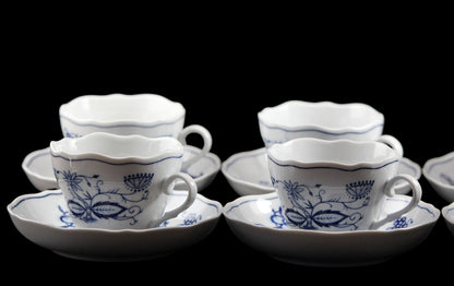 Set of white ceramic teacups and saucers with blue floral patterns on a dark background