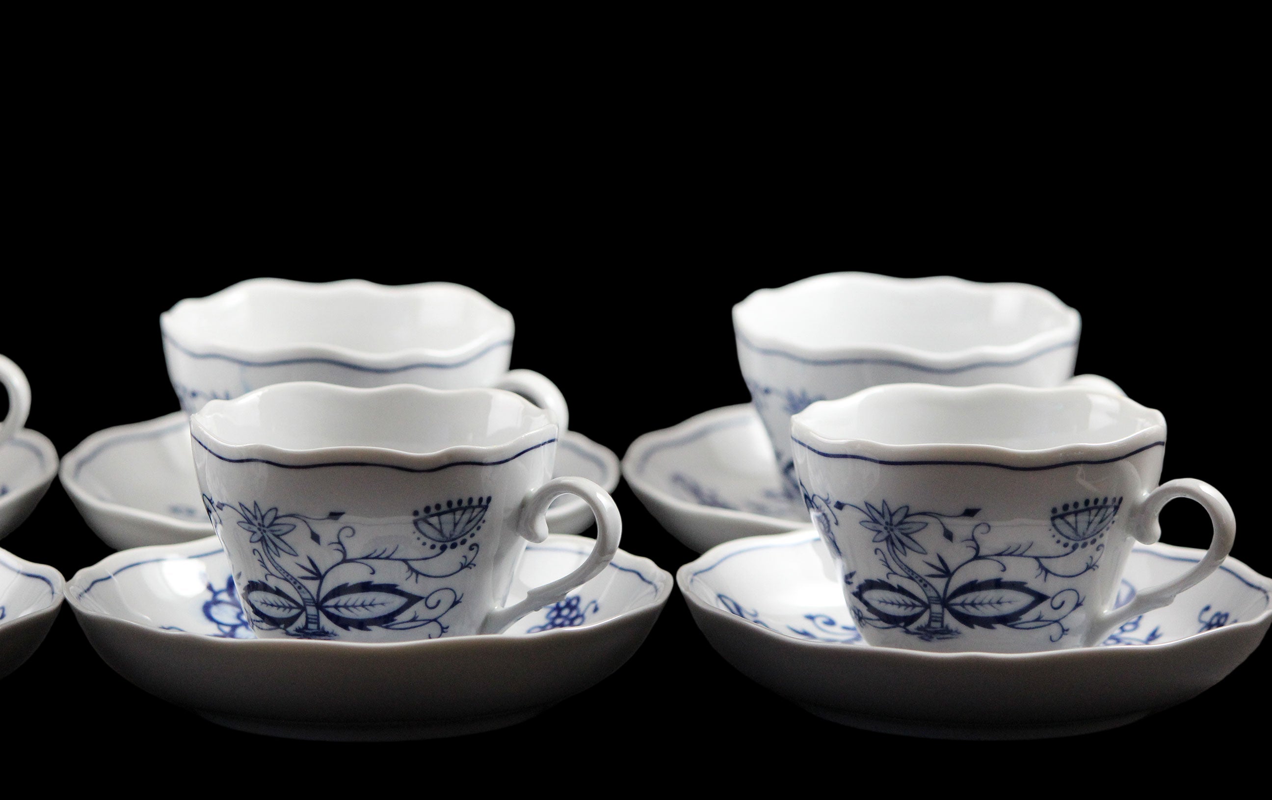 Set of white ceramic cups and saucers with blue floral patterns on a dark background