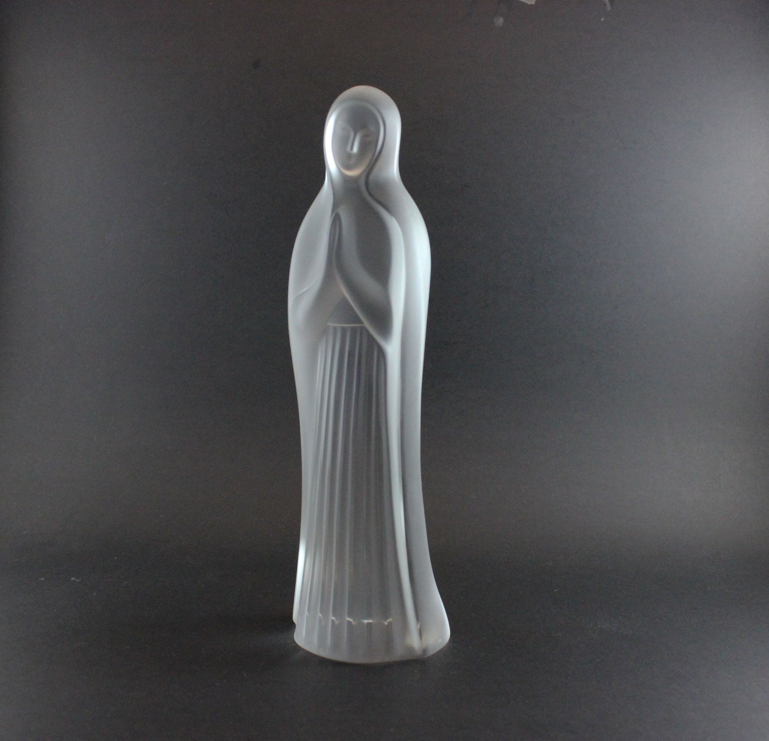 Clear glass statue of a standing figure on a dark background
