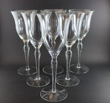 Set of six clear wine glasses with textured stems on a dark background
