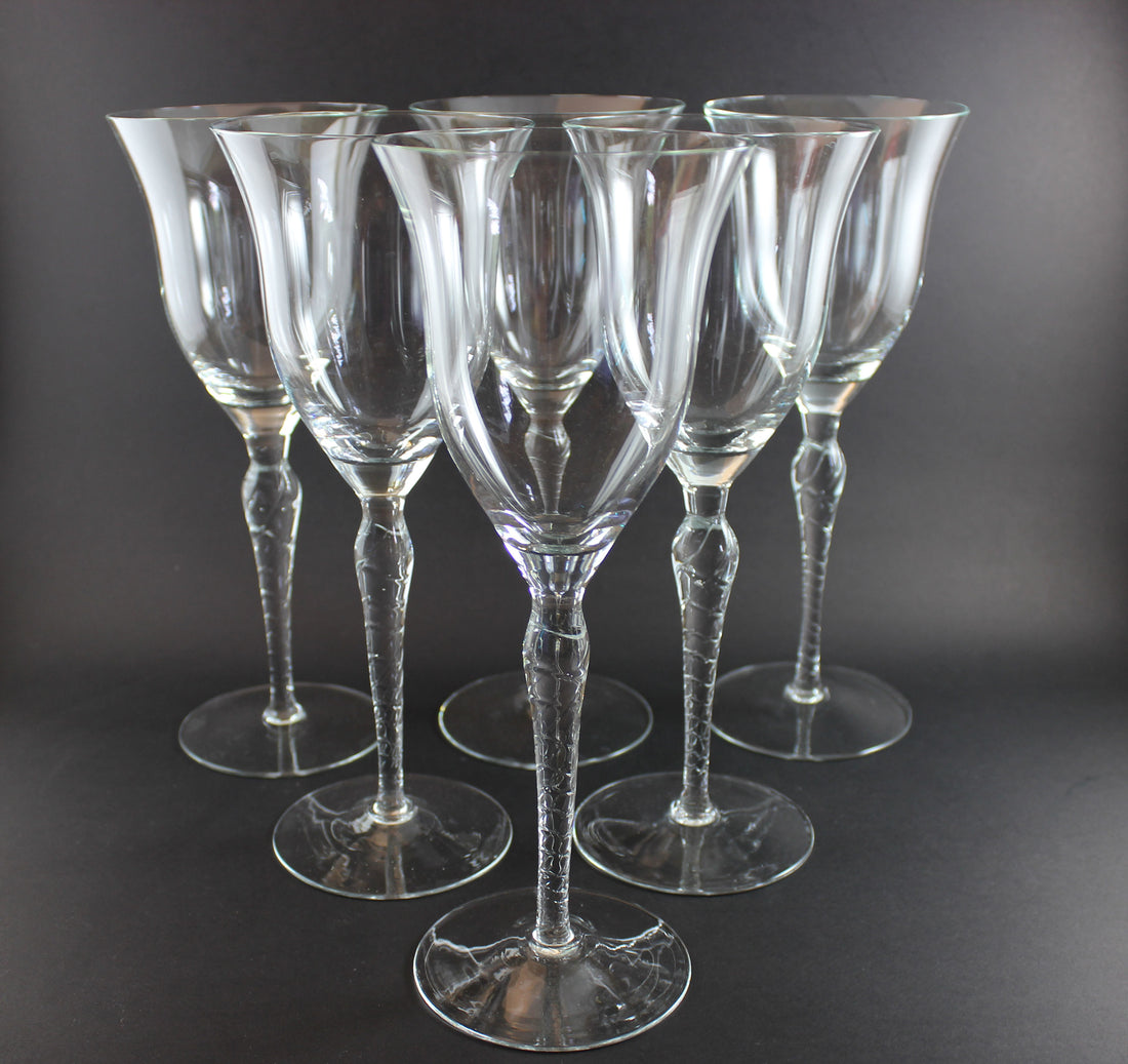 Set of six clear wine glasses with textured stems on a dark background
