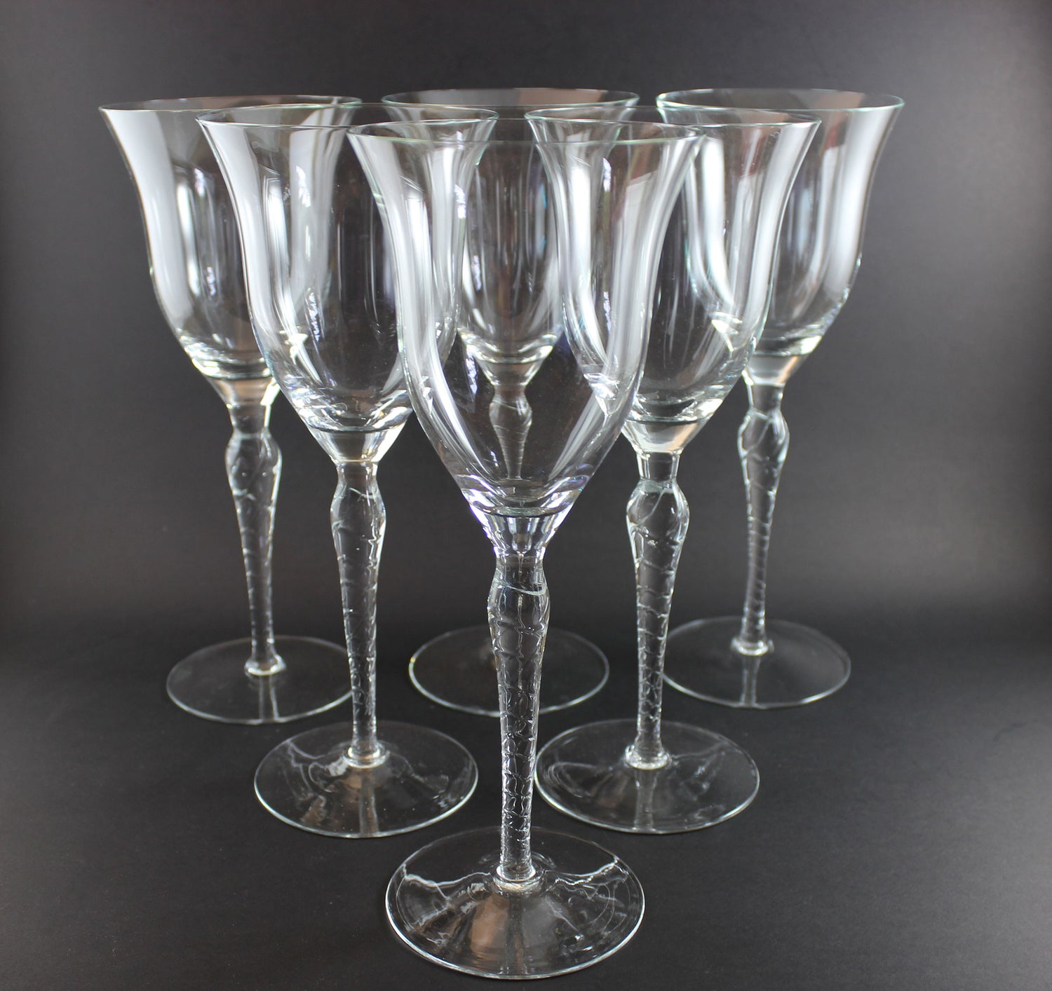 Set of six clear wine glasses with textured stems on a dark background
