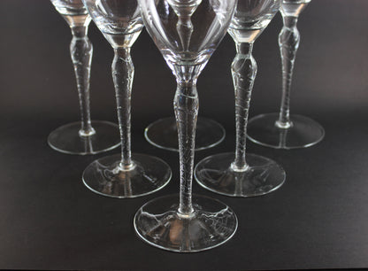 Set of six clear wine glasses with textured stems on a black background