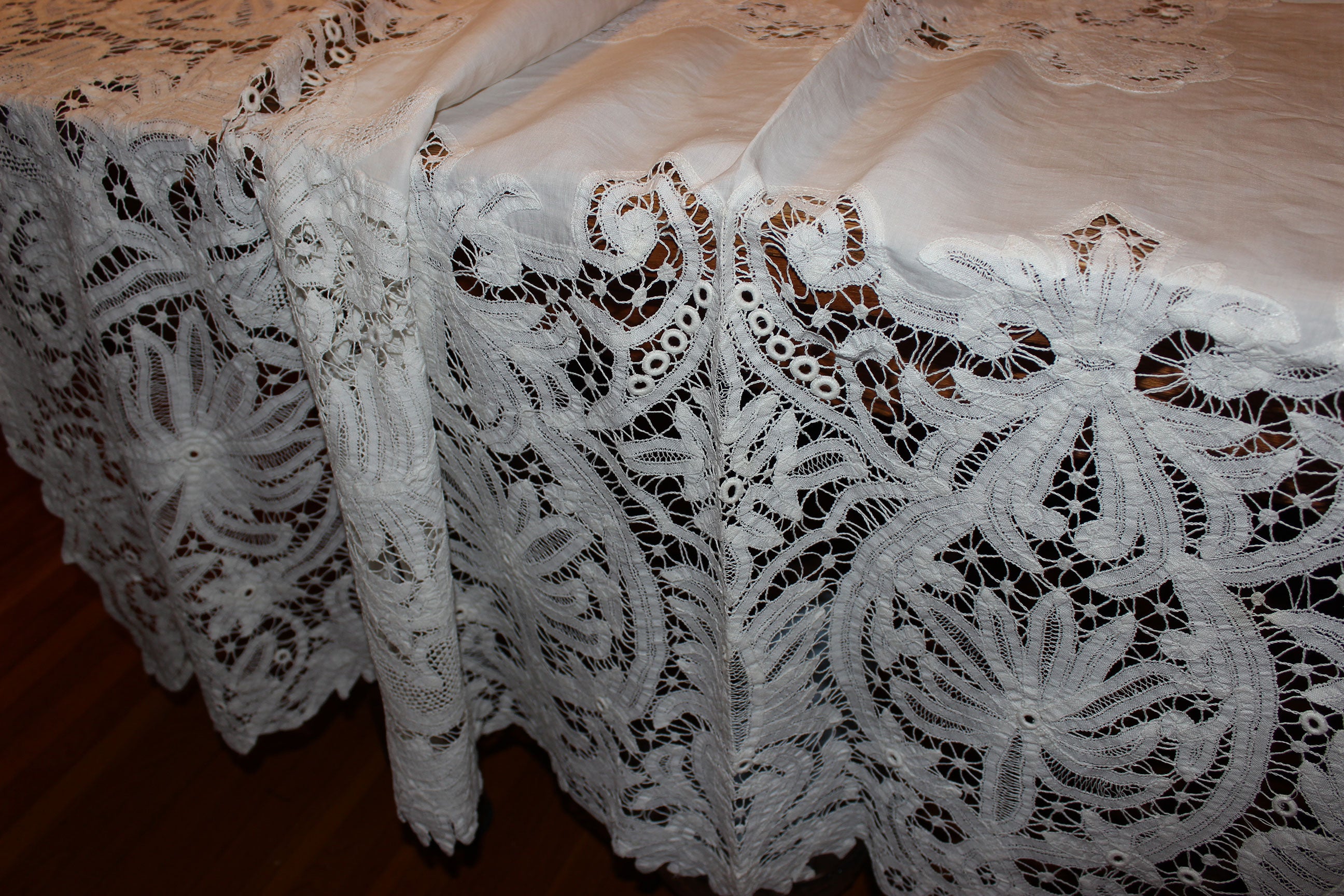 Close-up of a lace tablecloth with intricate patterns on a wooden surface.