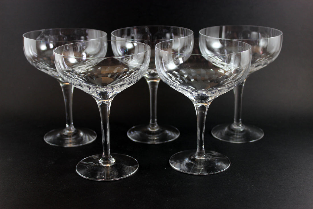 Set of six clear champagne coupe glasses on a black background