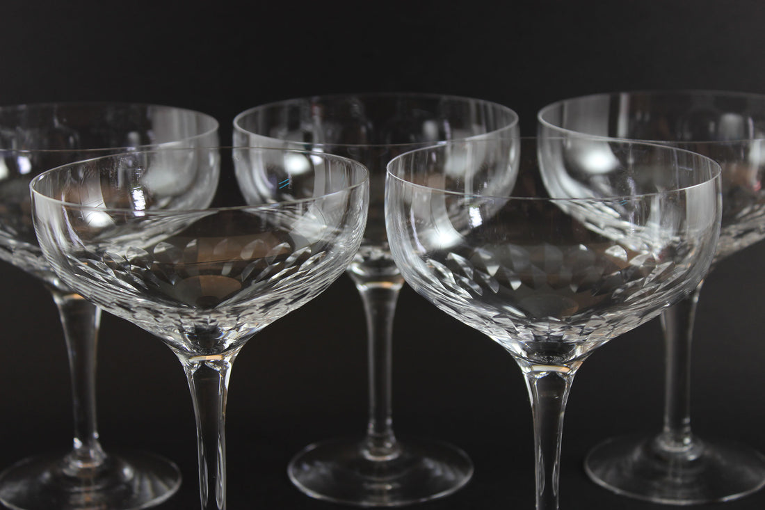 Set of six clear champagne coupe glasses on a black background