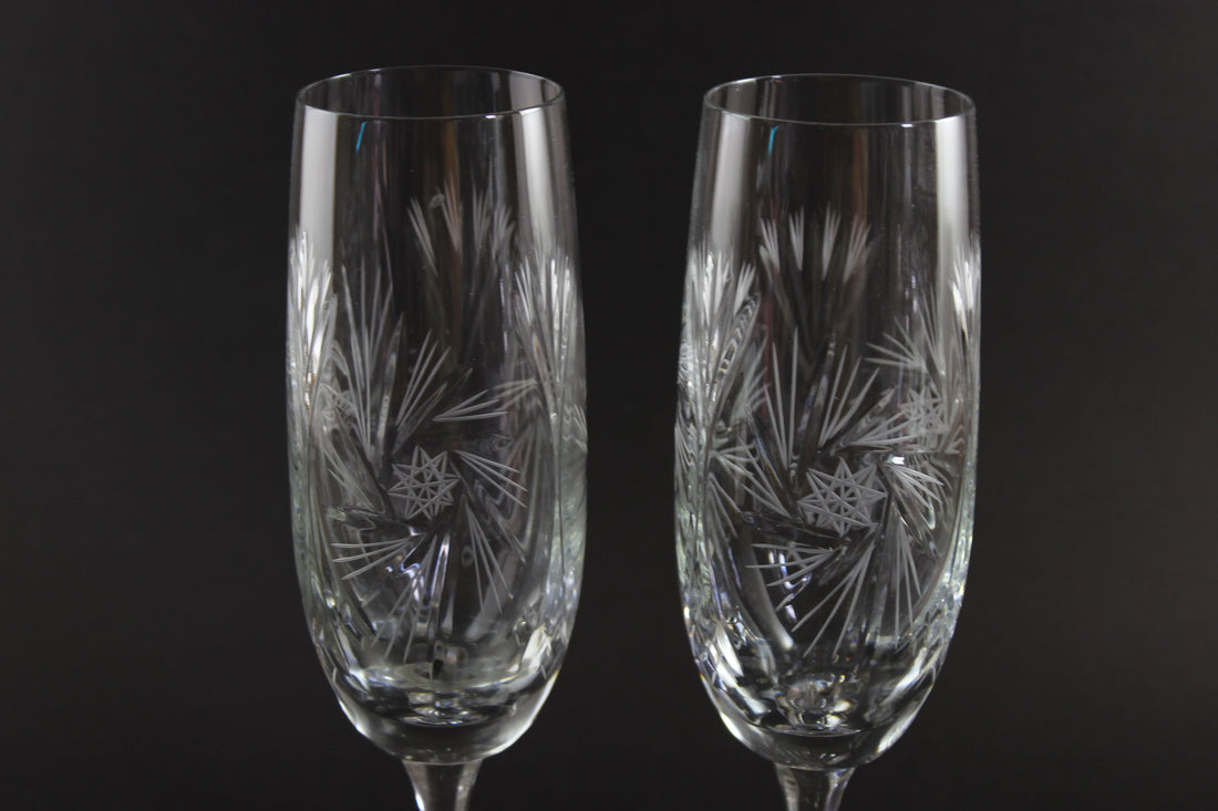 Two crystal champagne flutes with cut pinwheel design on a black background