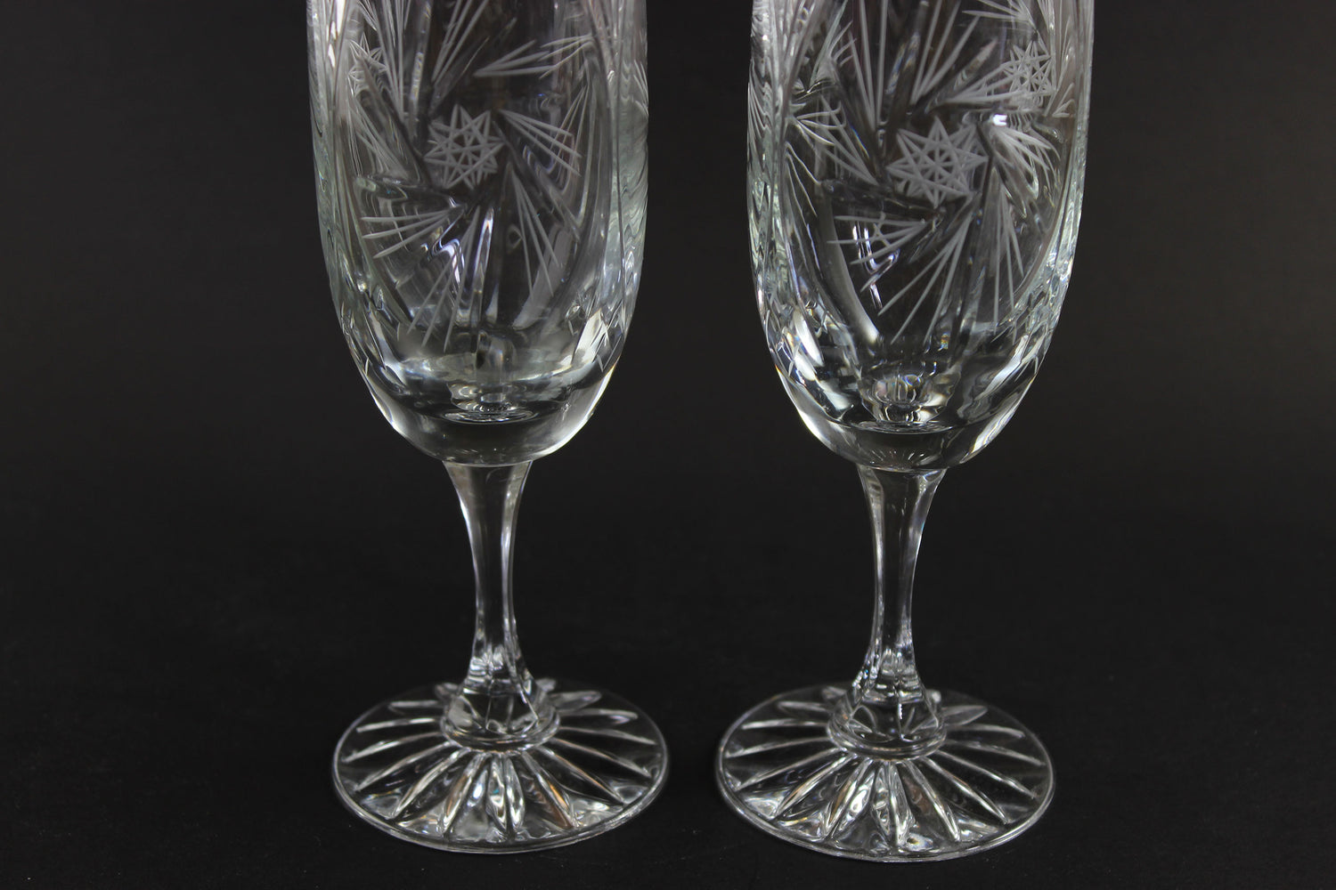 Two crystal champagne flutes with cut pinwheel design on a black background