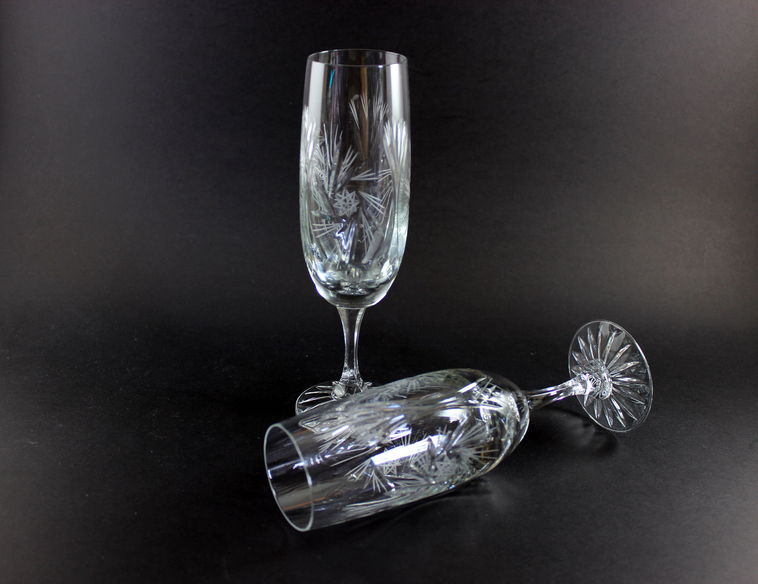 Two crystal champagne flutes with cut pinwheel design on a black background