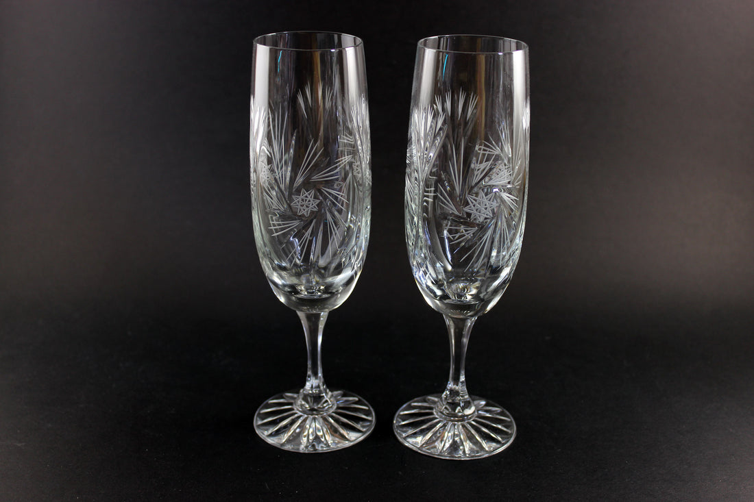 Two crystal champagne flutes with cut pinwheel design on a black background