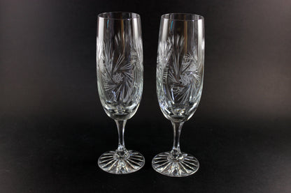 Two crystal champagne flutes with cut pinwheel design on a black background
