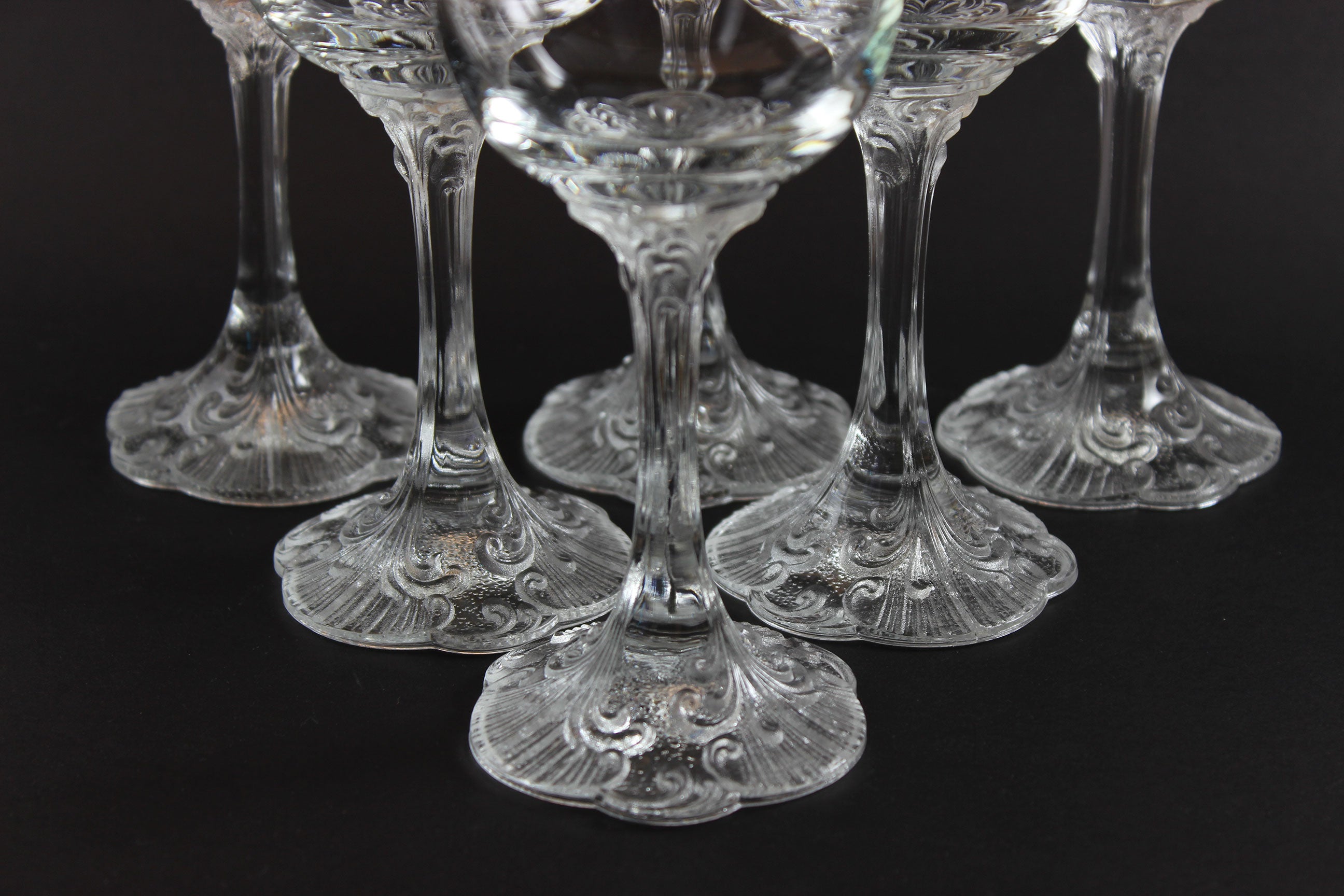 Set of clear glass cocktail glasses with intricate designs on a black background