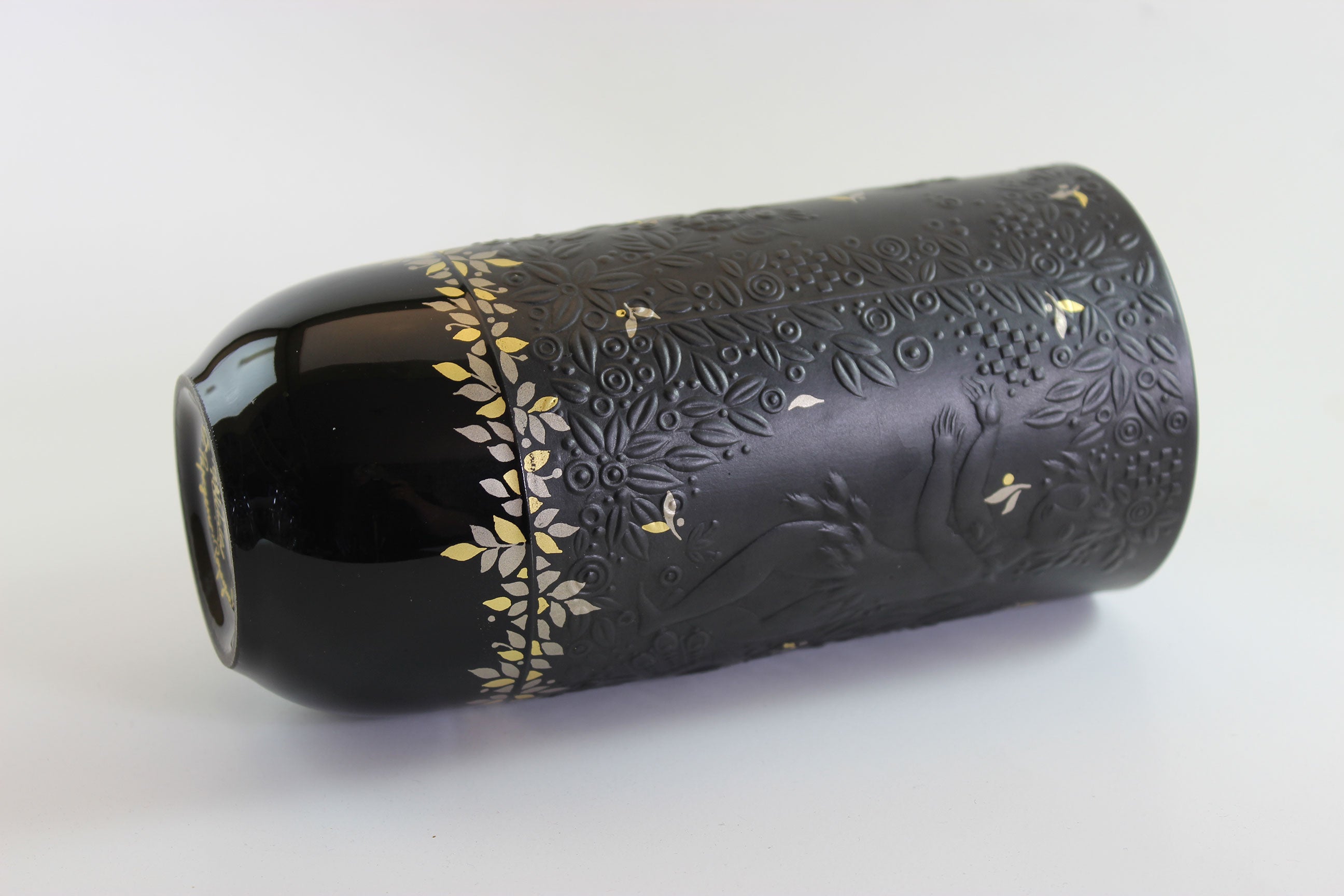 Black cylindrical product with gold floral patterns on a white background