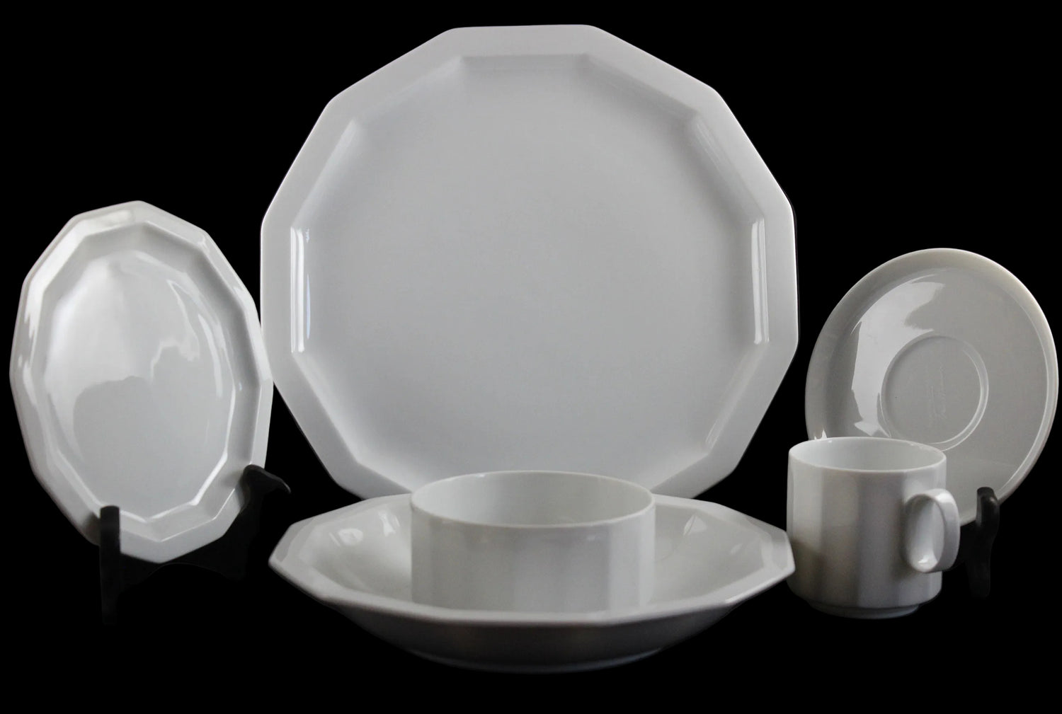 Six piece white porcelain dinnerware including plates, bowls, cup and saucer on a black background