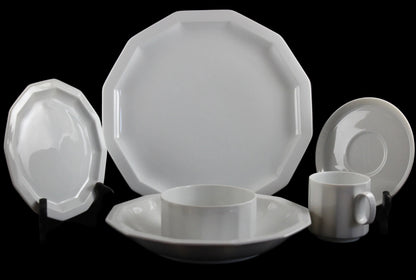 Six piece white porcelain dinnerware including plates, bowls, cup and saucer on a black background