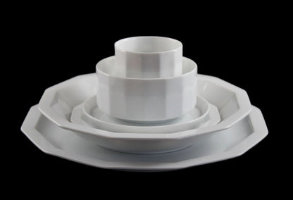 Six piece white porcelain dinnerware including plates, bowls, cup and saucer on a black background