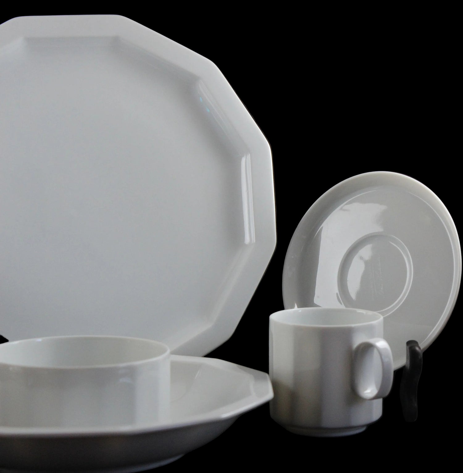 Six piece white porcelain dinnerware including plates, bowls, cup and saucer on a black background