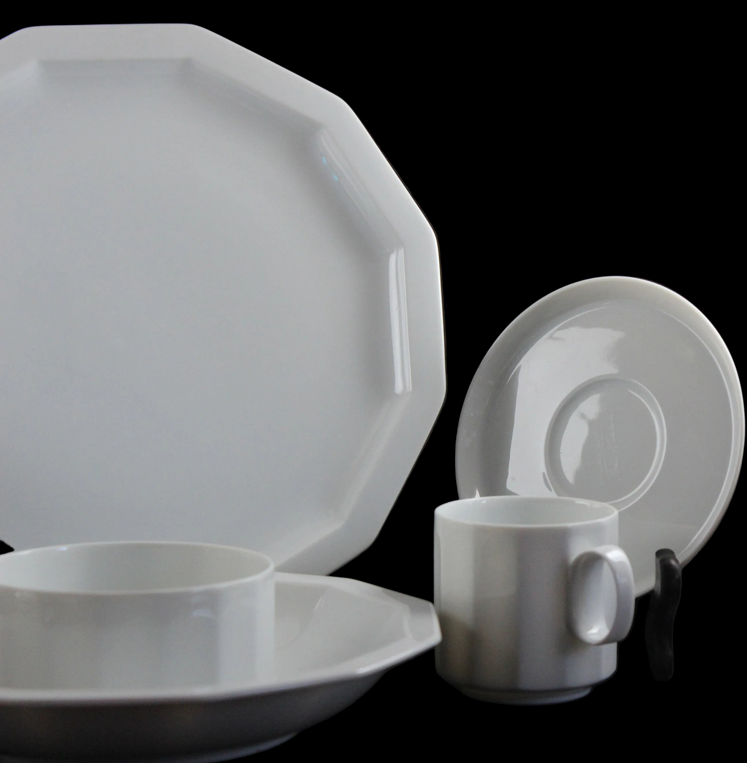 Six piece white porcelain dinnerware including plates, bowls, cup and saucer on a black background