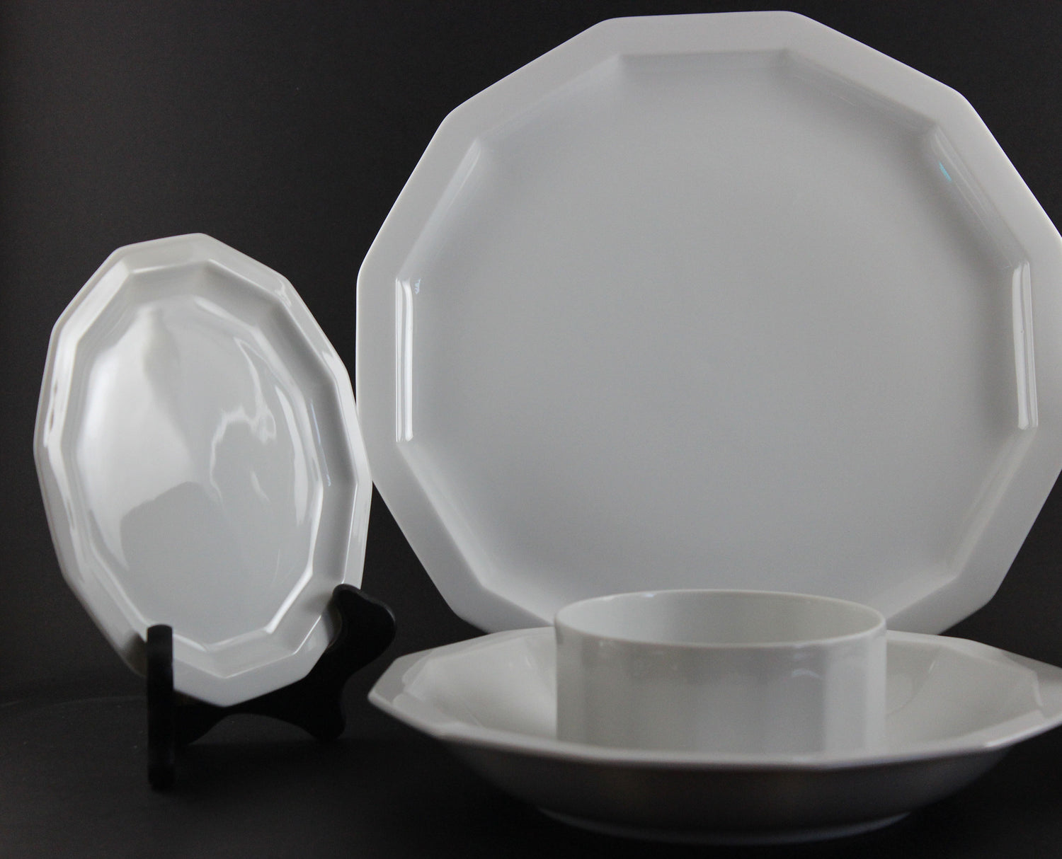 Six piece white porcelain dinnerware including plates, bowls, cup and saucer on a black background