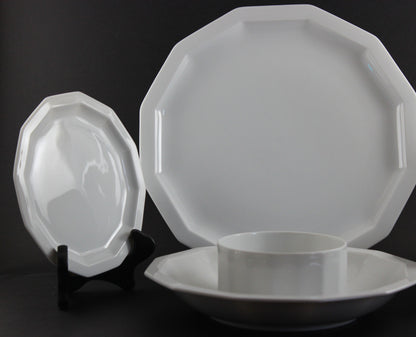 Six piece white porcelain dinnerware including plates, bowls, cup and saucer on a black background