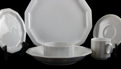 Six piece white porcelain dinnerware including plates, bowls, cup and saucer on a black background