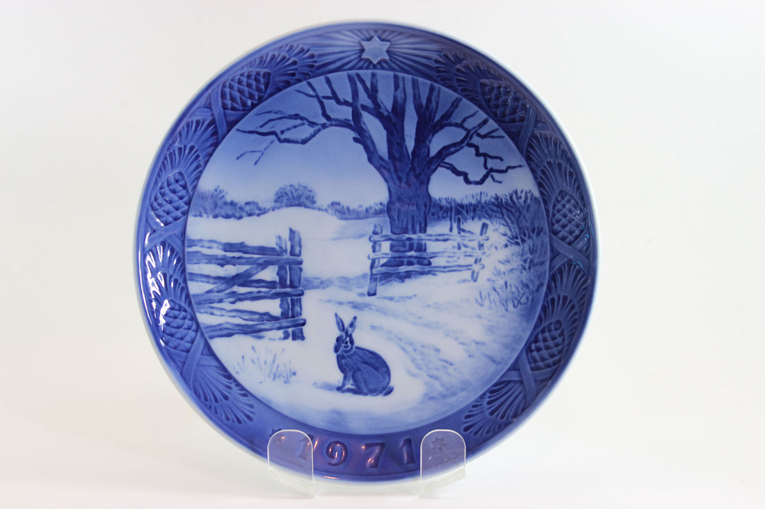1971 Blue and white ceramic plate with a winter scene of a rabbit and tree, on a white background.