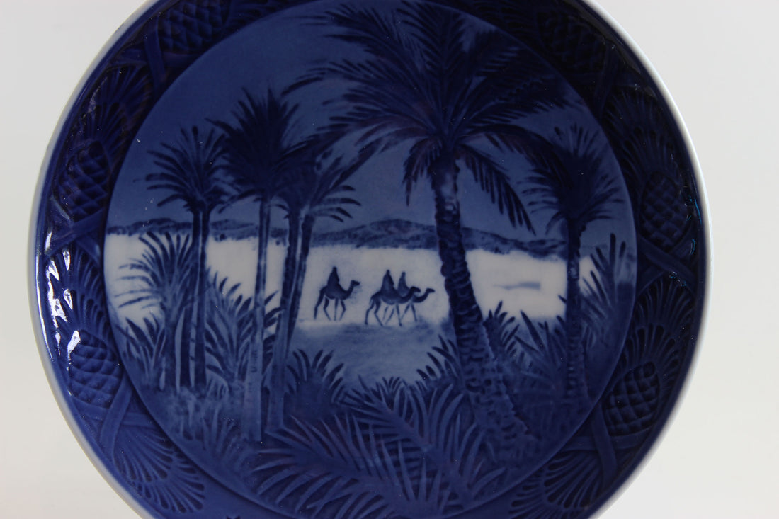 Blue ceramic plate with a scenic design of camels and palm trees on a white background