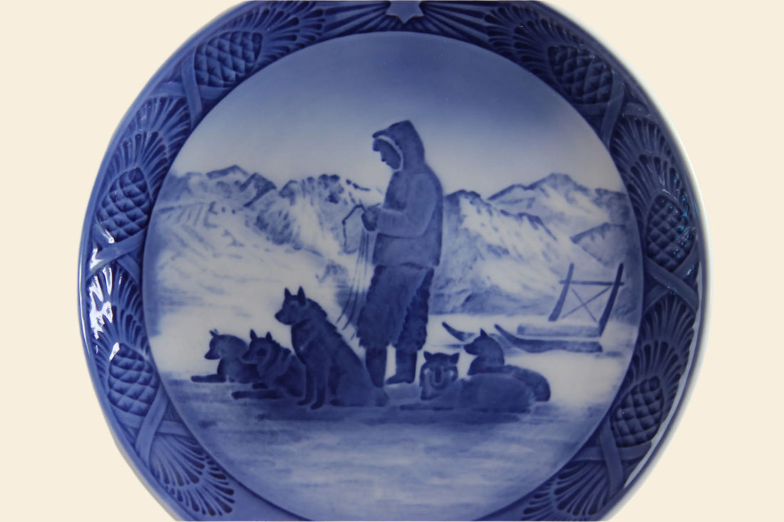 Decorative plate with a blue and white design of a person with dogs in a snowy landscape.