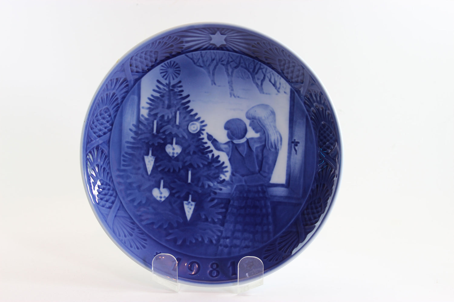 Decorative blue plate with a Christmas scene of a mother and child admiring a Christmas tree.