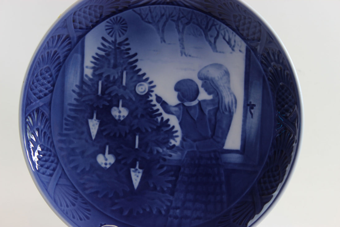 Decorative blue plate with a Christmas scene of a mother and child admiring a Christmas tree.