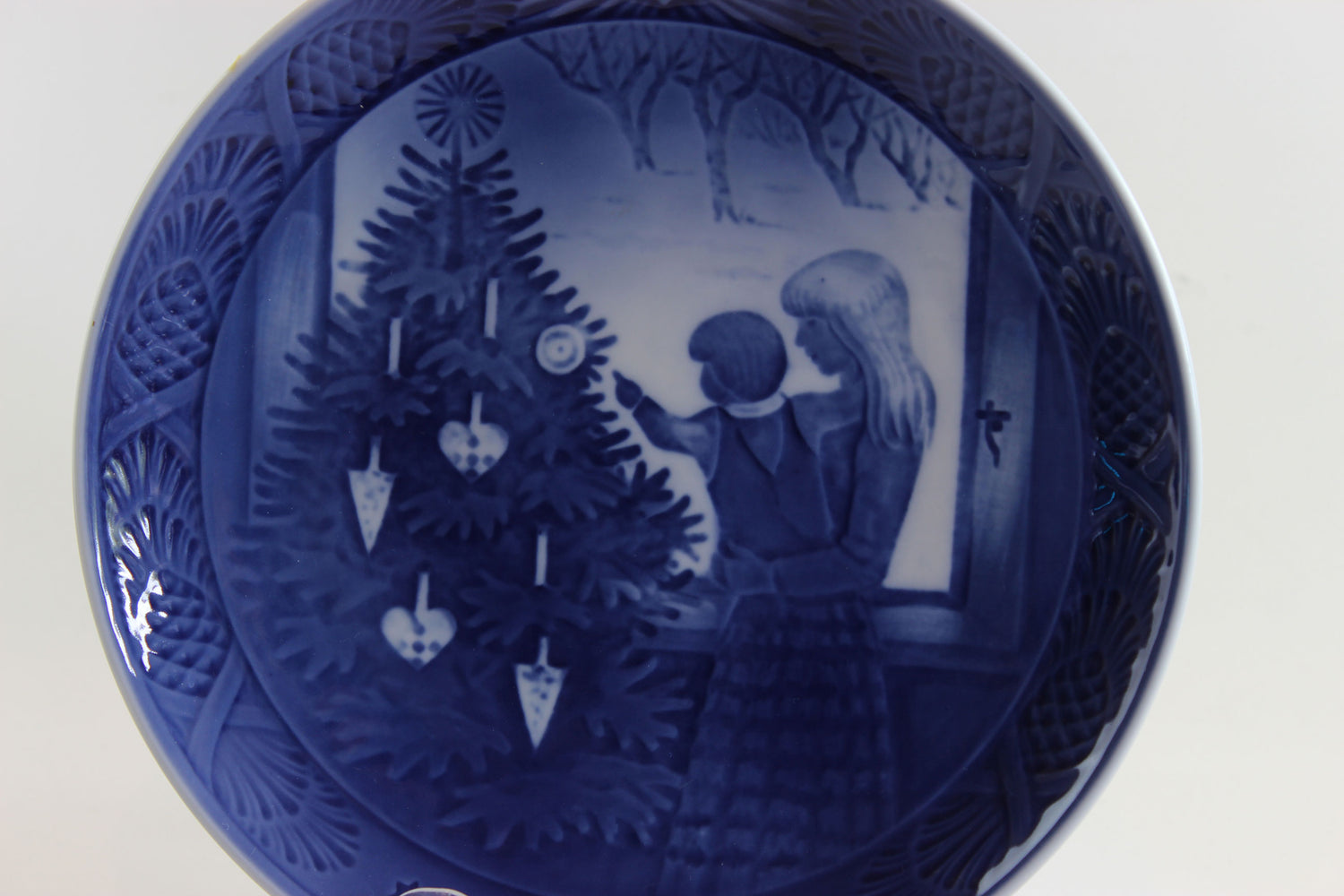 Decorative blue plate with a Christmas scene of a mother and child admiring a Christmas tree.