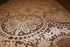 Close-up of a lace tablecloth with intricate patterns on a wooden surface.