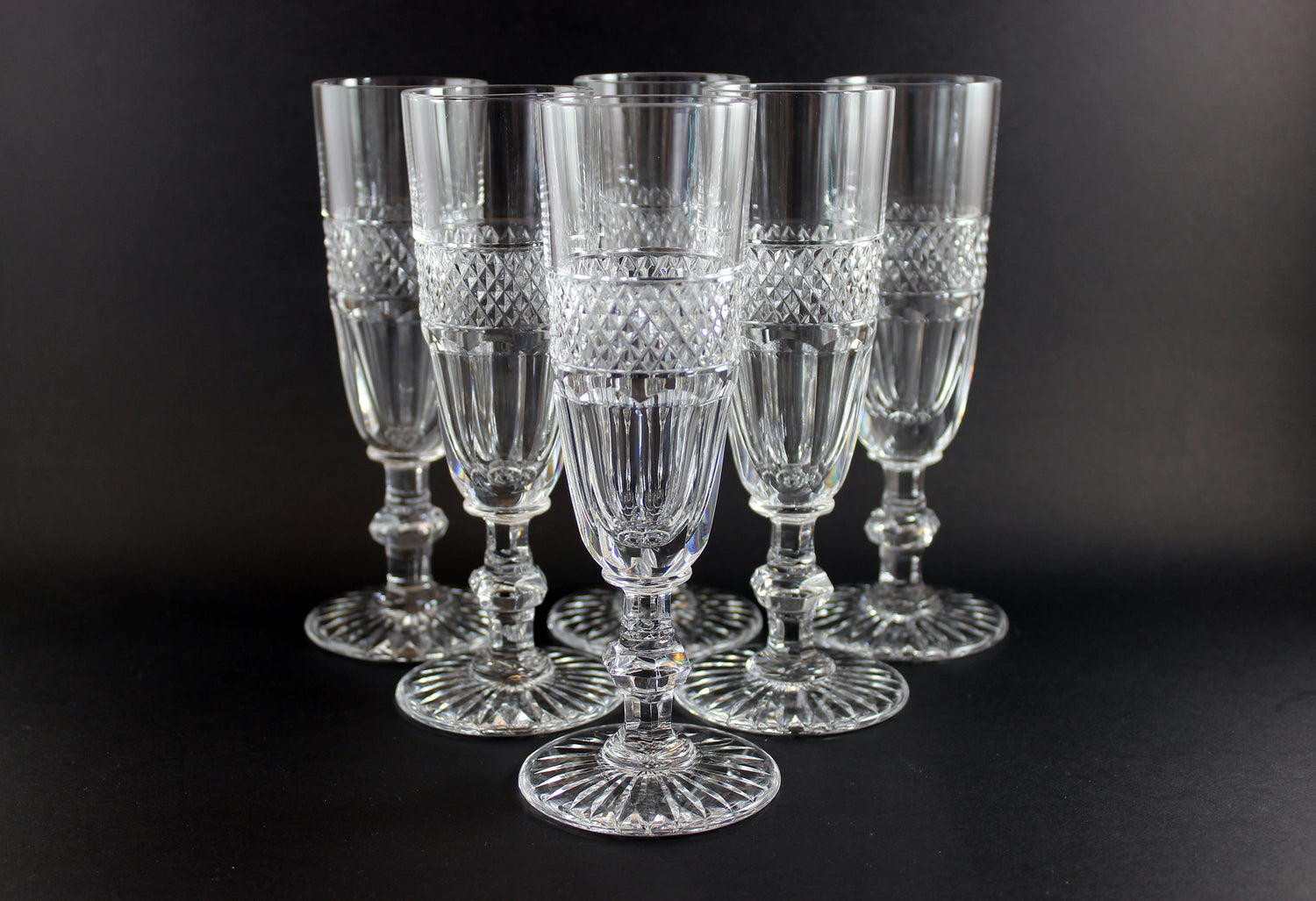 Set of six crystal glasses with diamond cut pattern on a black background