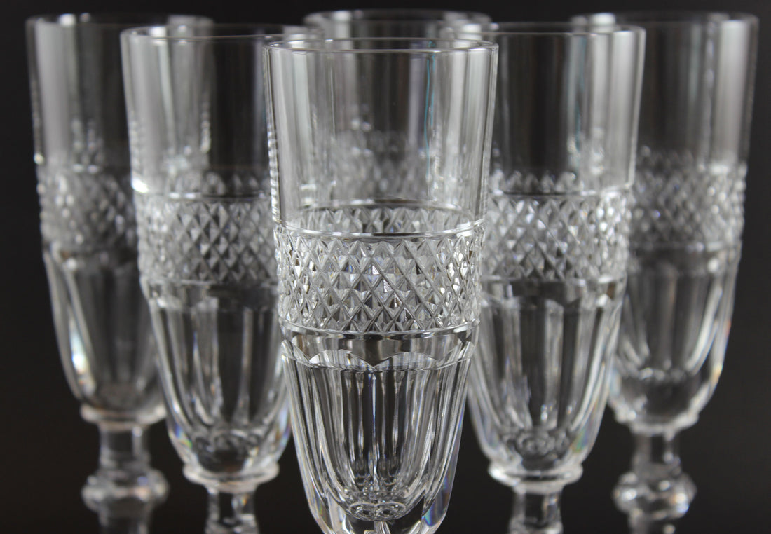 Set of six crystal champagne flutes with diamond pattern on a black background