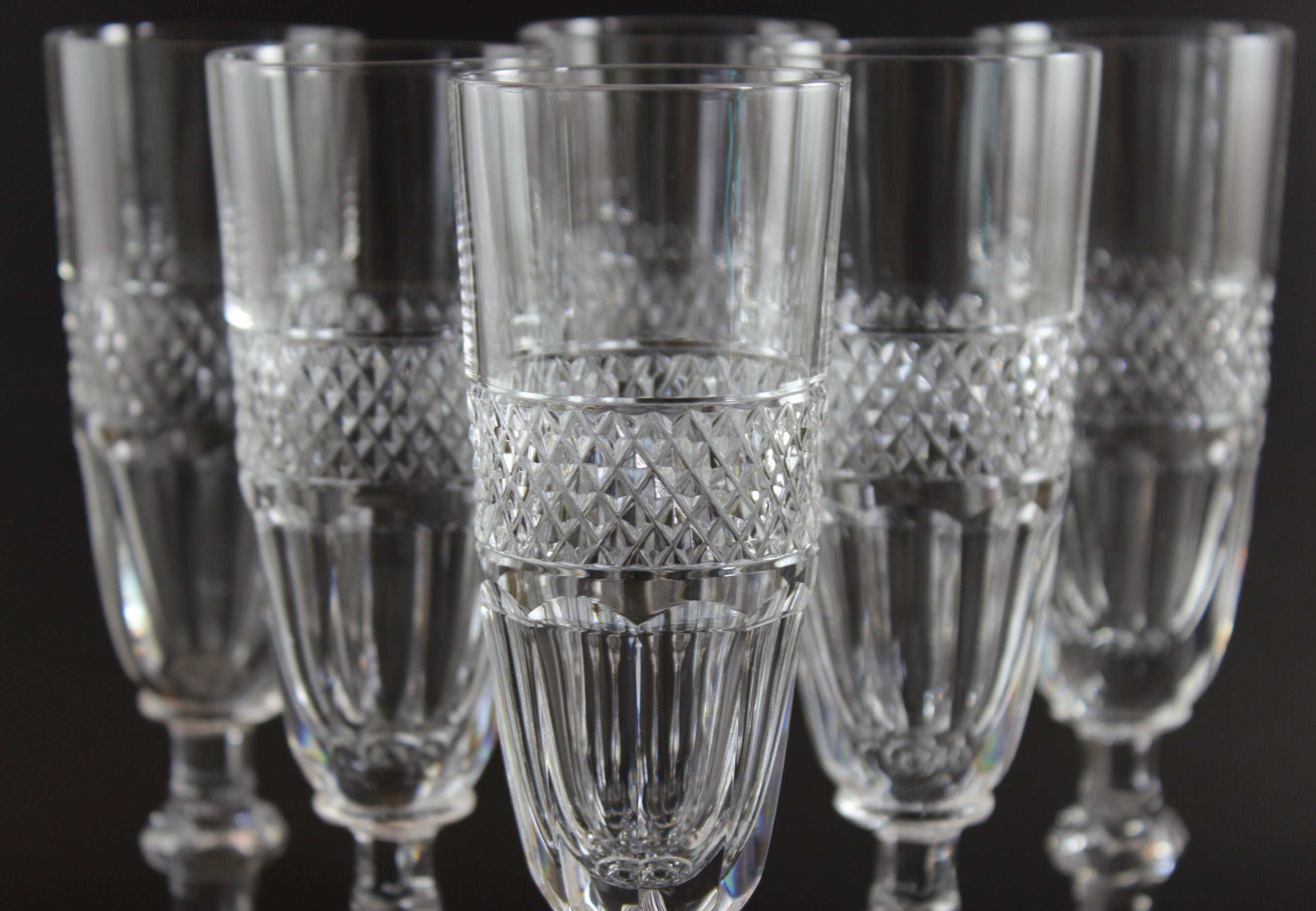 Set of six crystal champagne flutes with diamond pattern on a black background