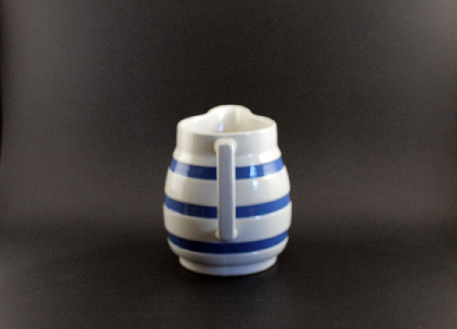 White ceramic pitcher with blue stripes on a black background