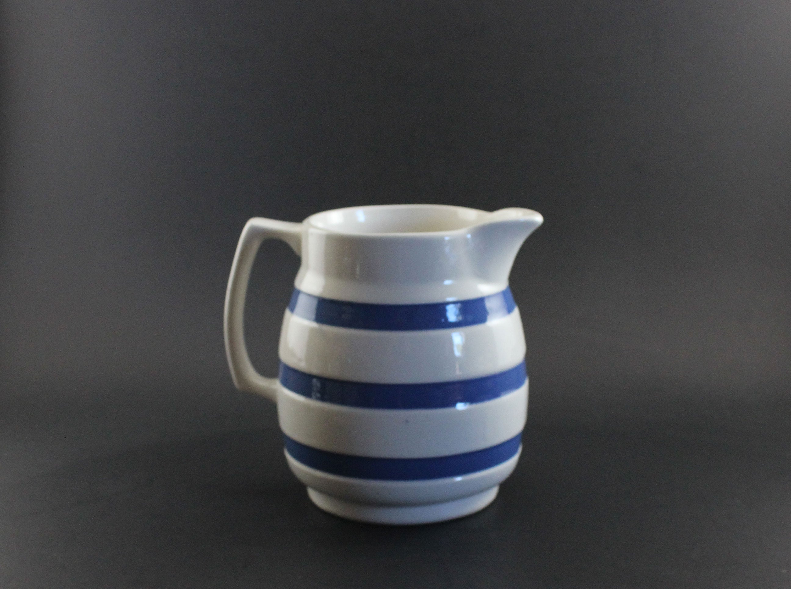 White ceramic pitcher with blue stripes on a dark background