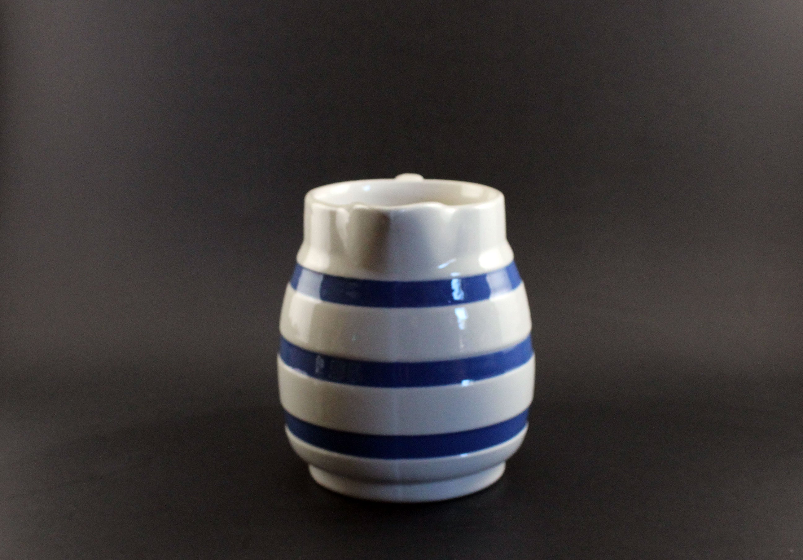 White ceramic pitcher with blue stripes on a dark background