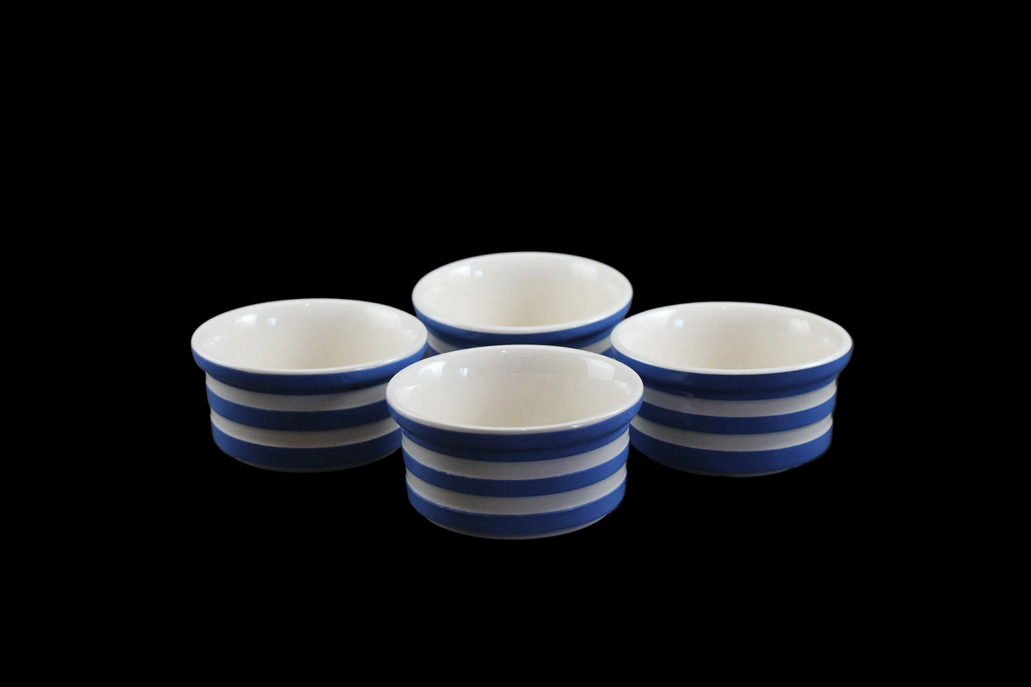Four ceramic ramekins with blue and white stripes on a dark background