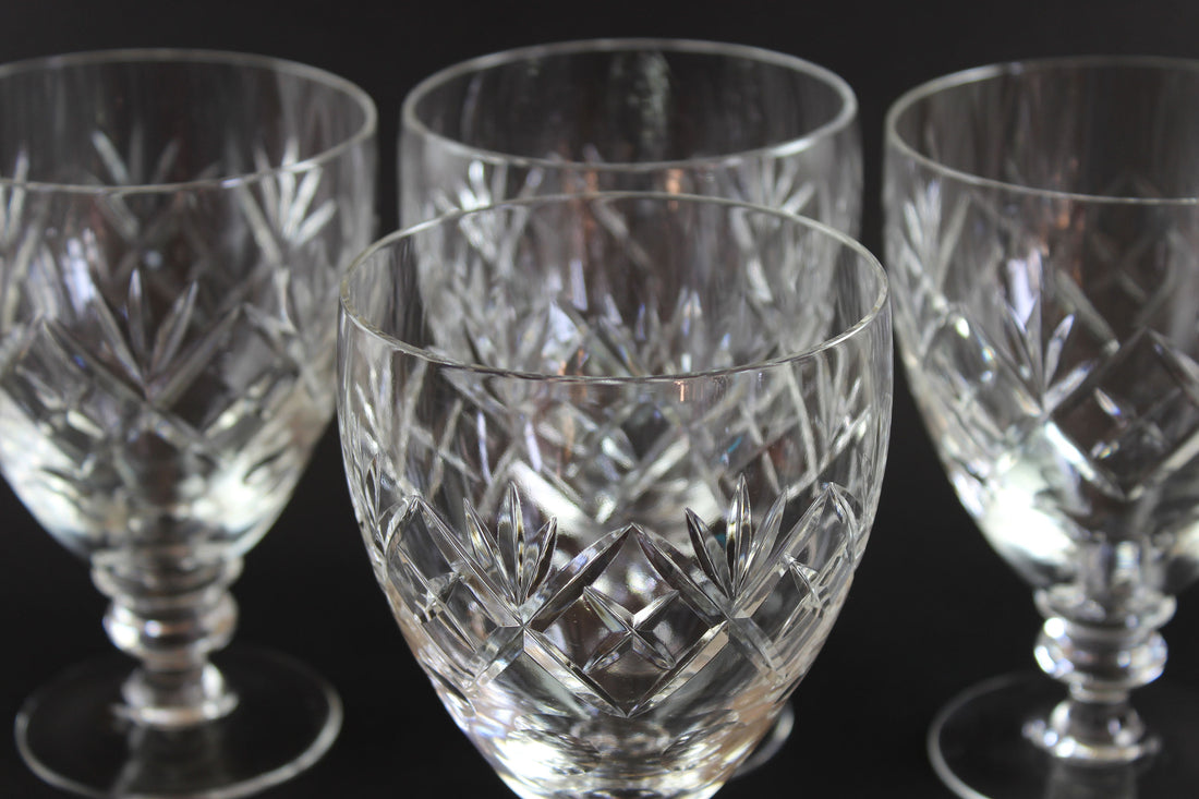 Set of four crystal glasses with intricate cut patterns on a black background